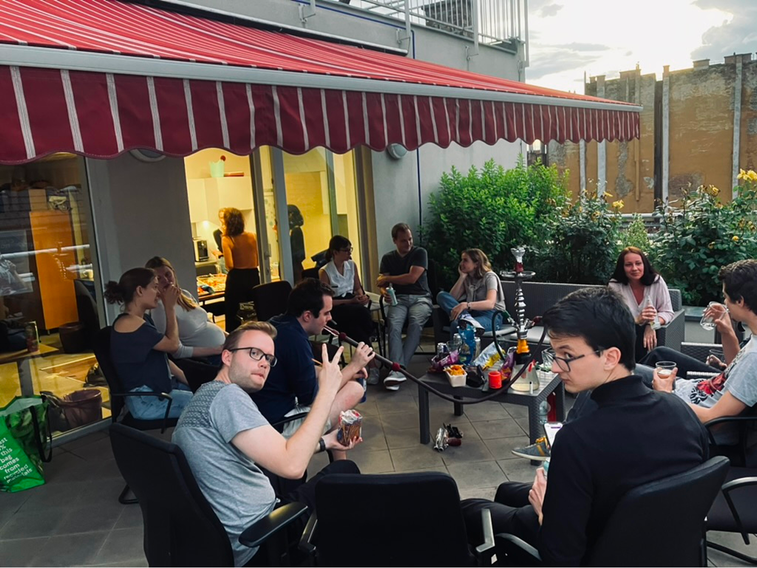 Fiatalok társasága egy teraszon, egyikük vízipipázik, mások beszélgetnek és italt fogyasztanak.