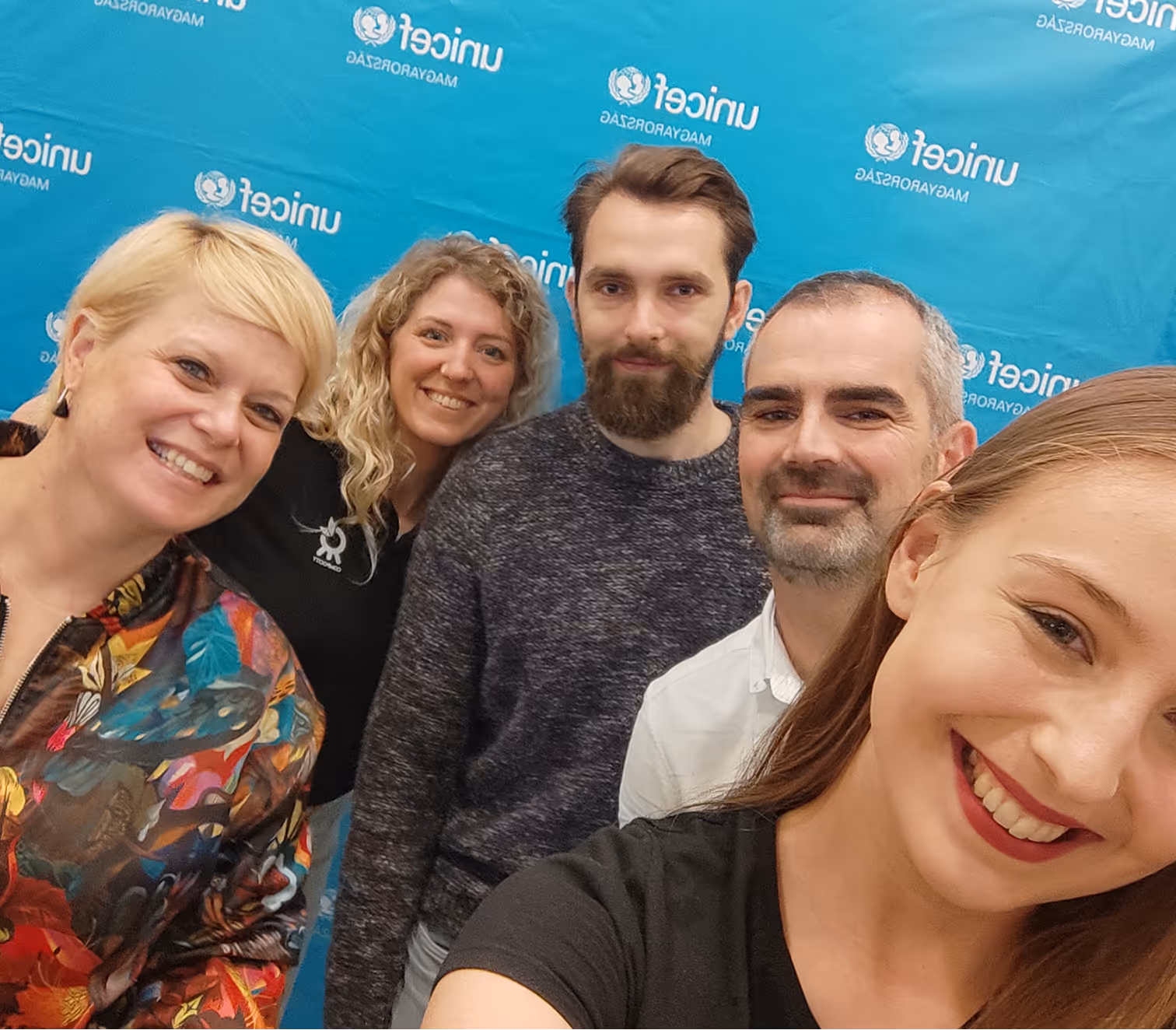 Öt mosolygó ember csoportképe kék UNICEF háttér előtt.