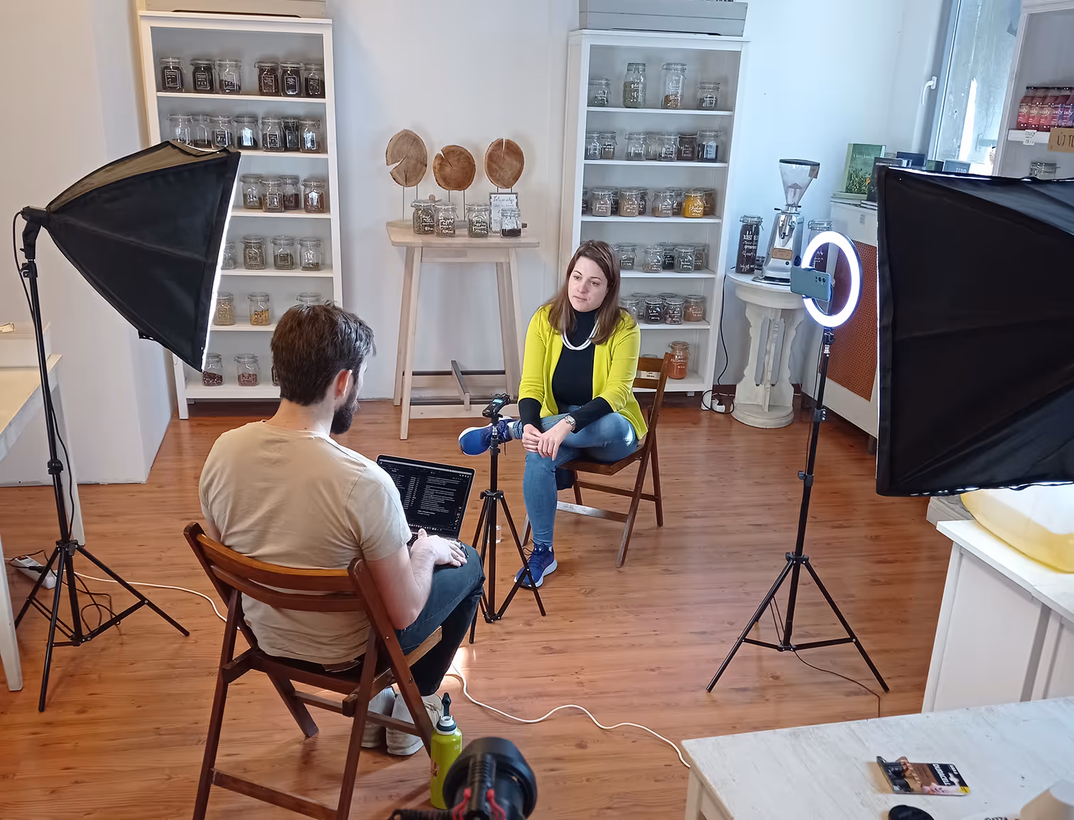 Nő beszélget egy férfival egy stúdióban, két softbox lámpa és egy gyűrűs lámpa világítja meg a teret.