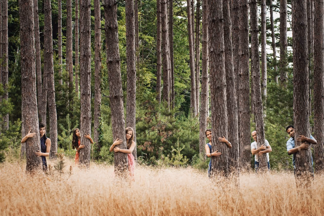 Hat ember ölel fákat egy erdőben, hosszú száraz fű és zöld fák között.