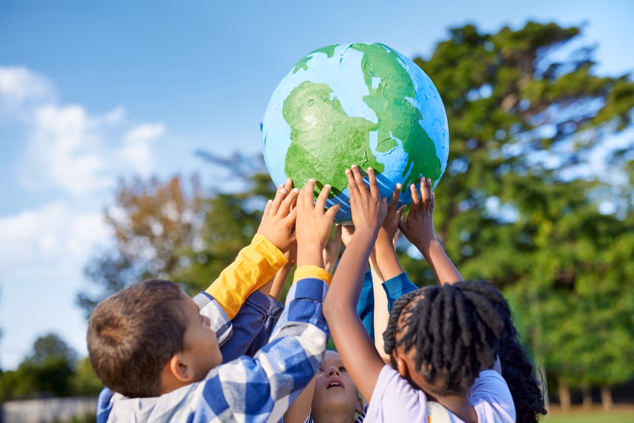 Gyerekek közösen tartanak egy földgömb modellt a levegőben napos szabadtéri környezetben.
