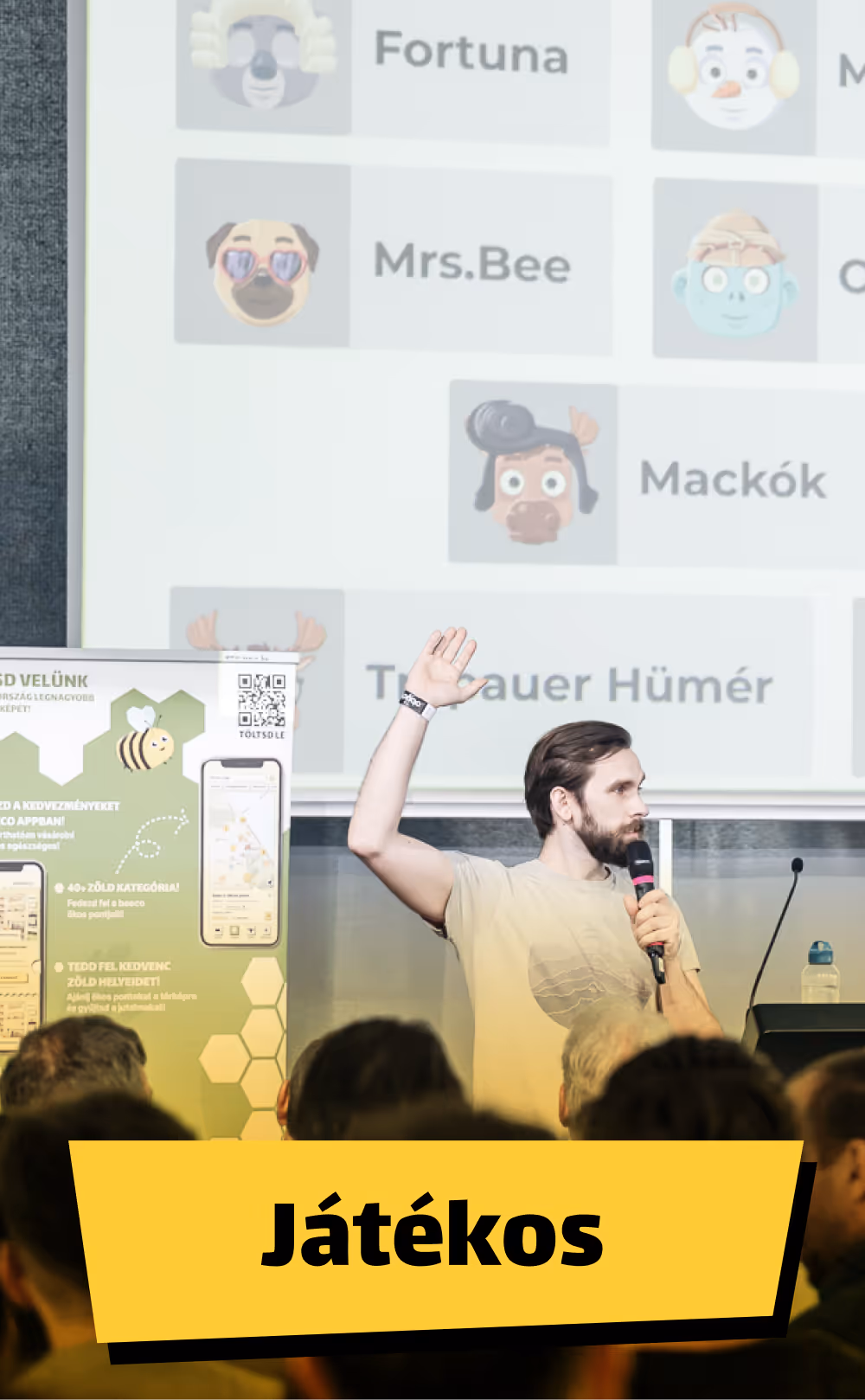 Egy férfi mikrofont tartva előad egy konferencián, háttérben egy prezentáció látható játékos karakterekkel, előtérben sárga színű Játékos felirat.