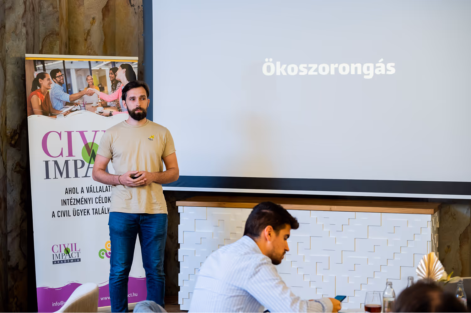Egy férfi előadást tart egy Civil Impact Akadémia molinó előtt, a vetítőn az Ökoszorongás felirat látható.