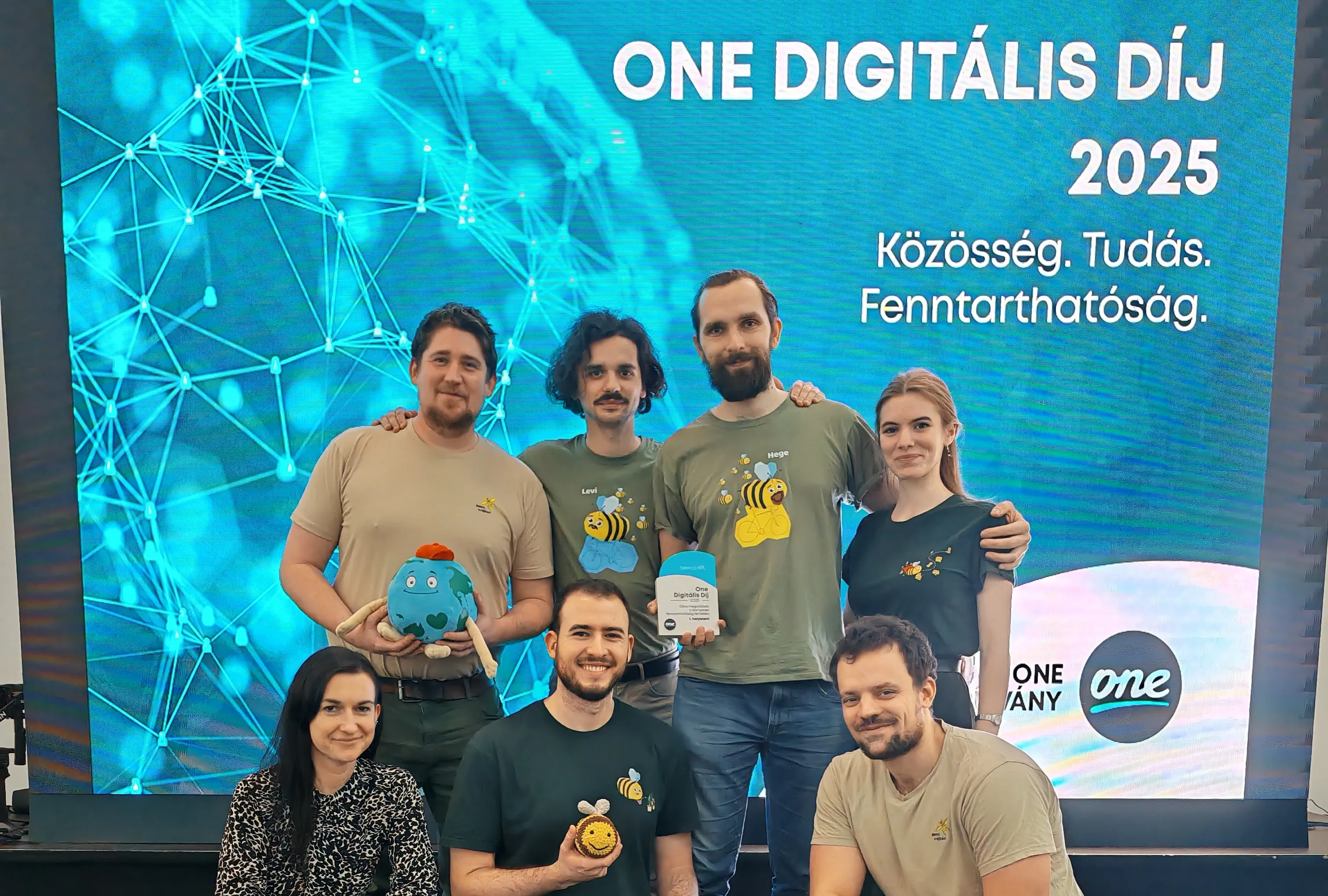 Hét ember csoportképe egy digitális díj átadón, háttérben a felirat: One Digitális Díj 2025, Közösség, Tudás, Fenntarthatóság.