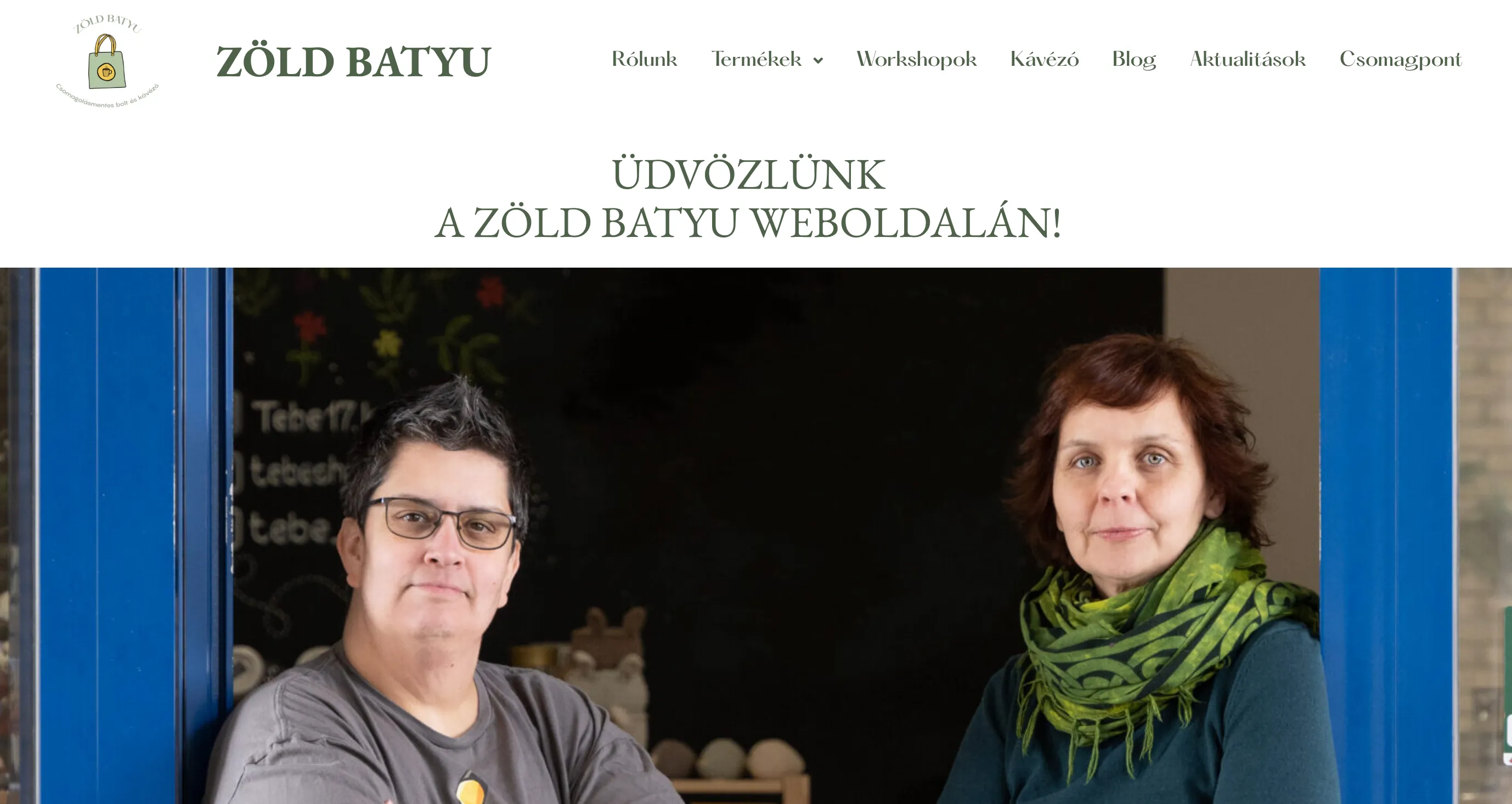 Két személy egy üzlet bejáratánál, a Zöld Batyu logóval és weboldal navigációs menüvel a háttérben.