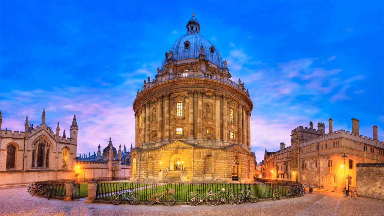 The Radcliffe Camera at Oxford University lit at dusk with bicycles parked in front.