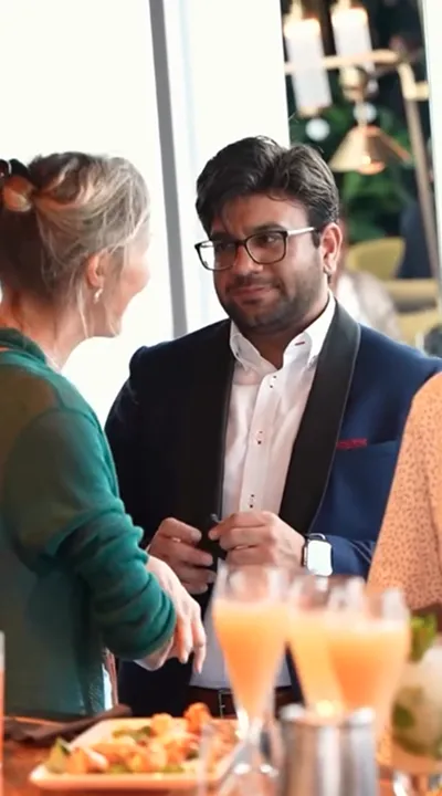 Man in glasses and suit listening to woman in green sweater during social gathering.