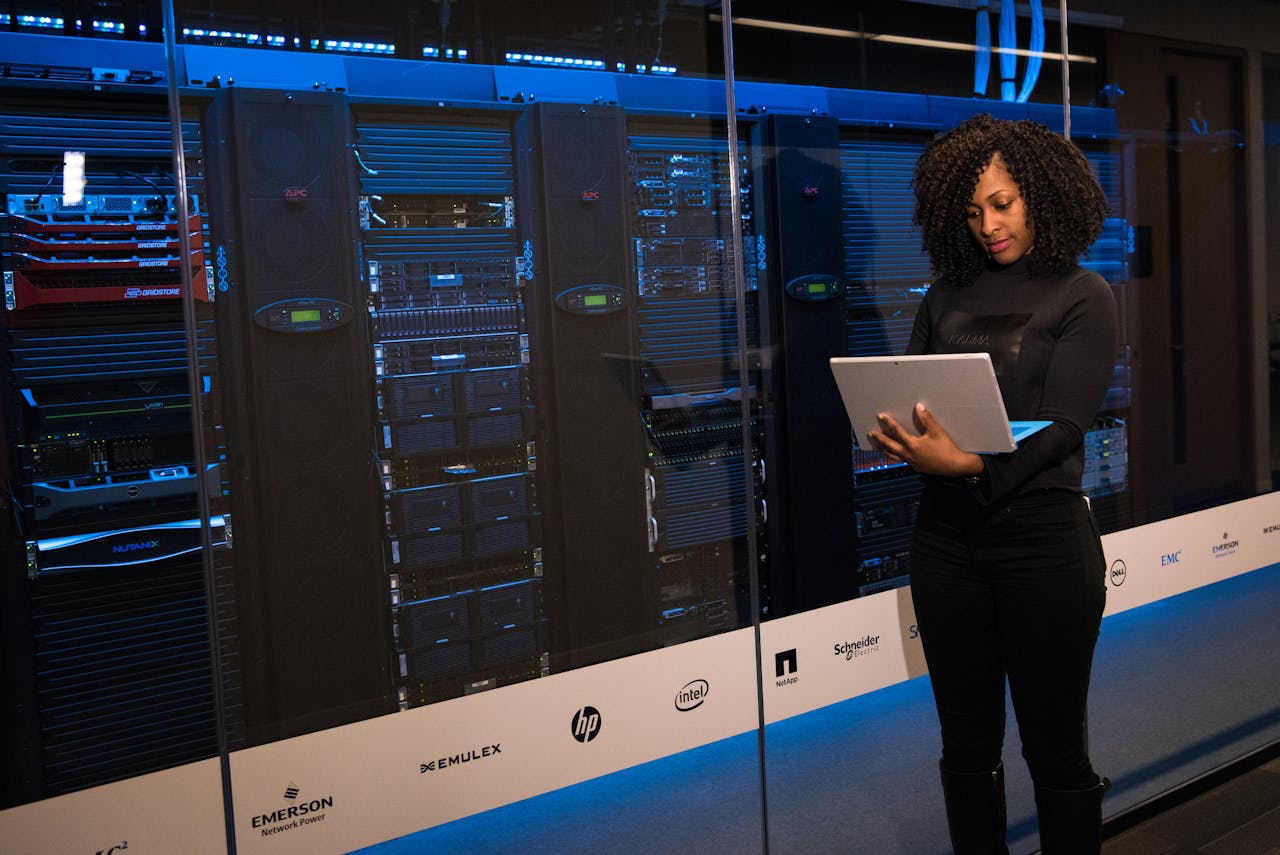 A female IT professional standing next to server racks, holding a tablet and overseeing the infrastructure. This symbolizes the critical process of IT systems modernization and data migration within the insurance sector.