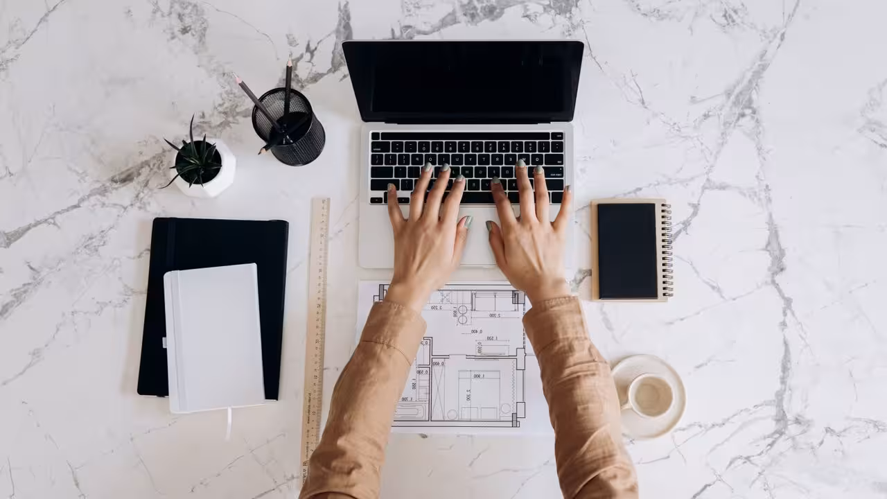 An overhead shot of hands holding a blueprint of a solar panel system and a calculator.