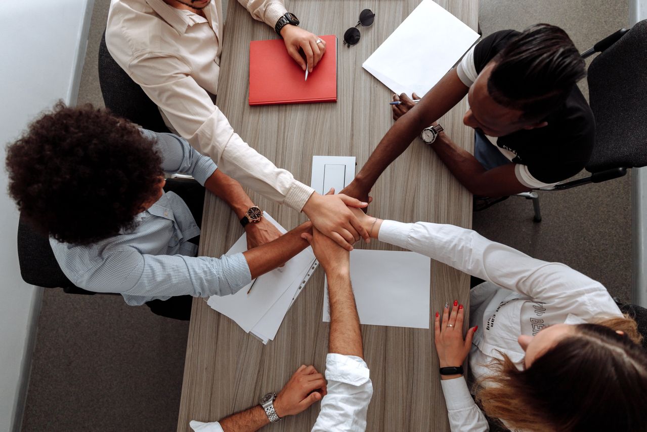  An overhead view of a diverse group of seven people in a circle, placing their hands together in the center.