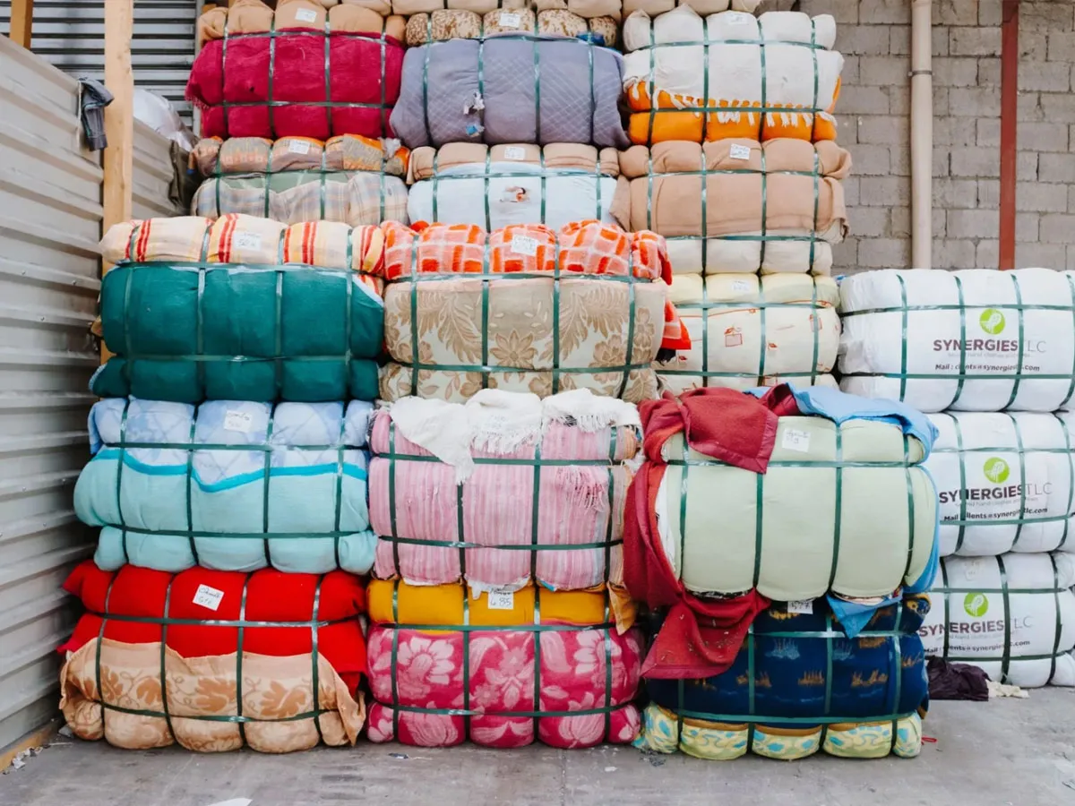 Stacks of colorful bundled blankets tied with green straps on a warehouse floor.