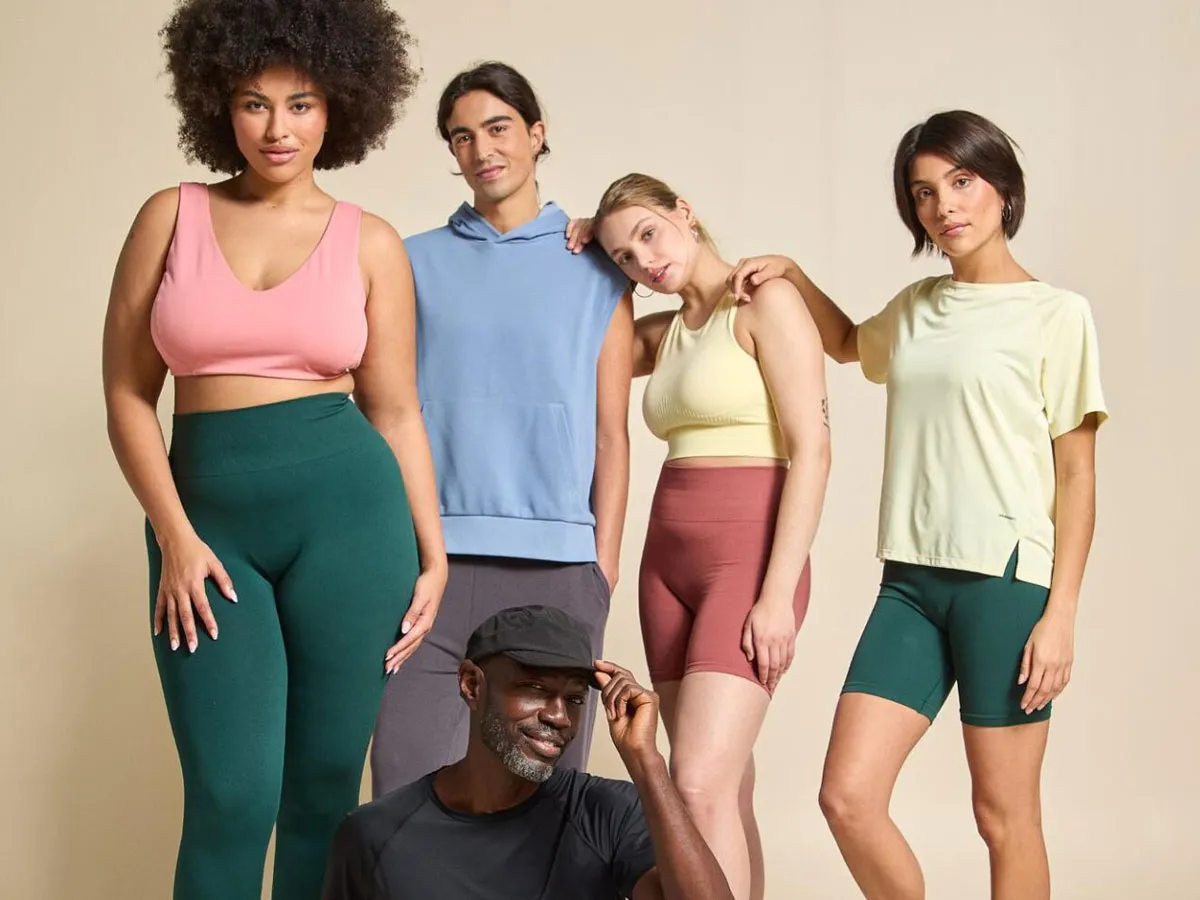 Diverse group of five adults posing in casual athletic wear against beige background.