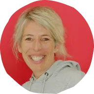 Smiling woman with blonde hair wearing a light gray hoodie against a red background.