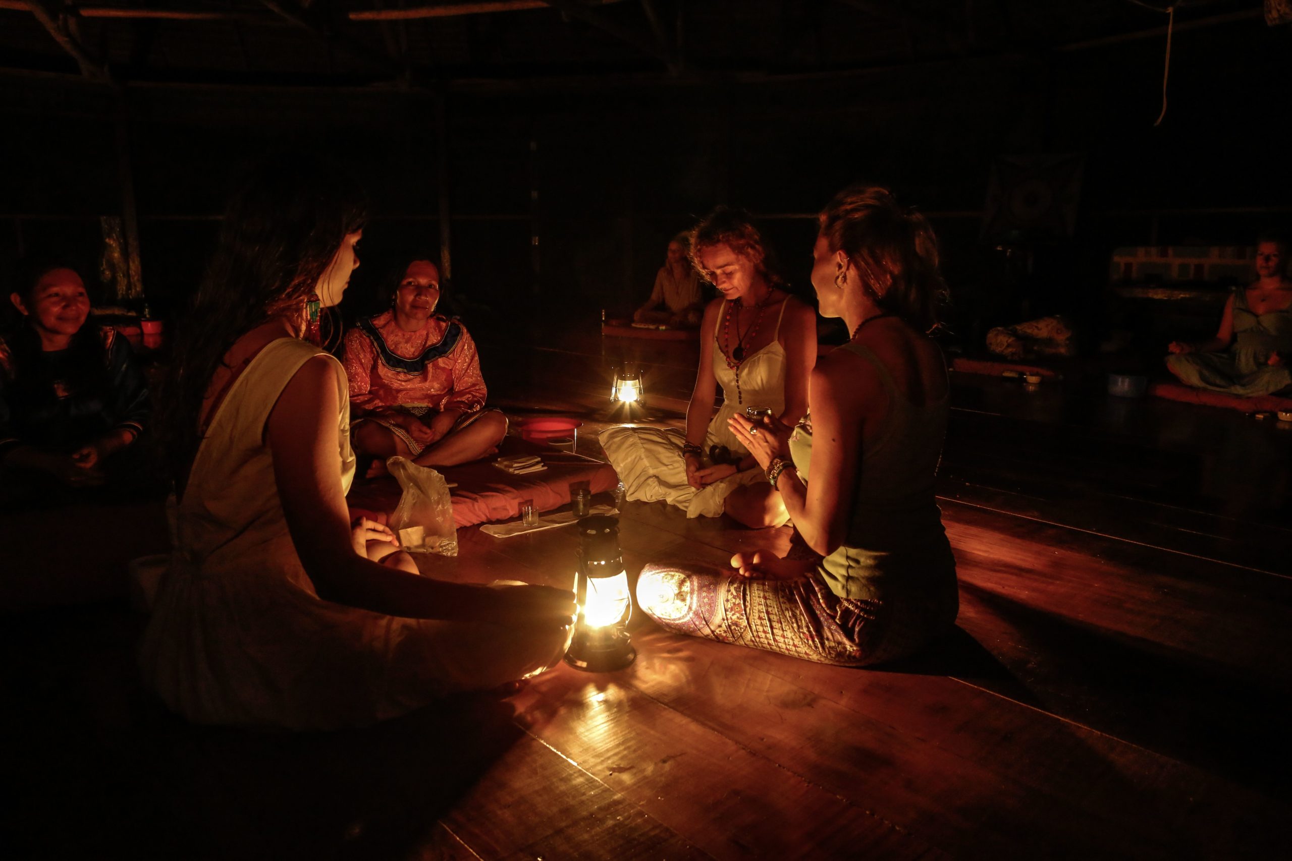 People sitting in a circle around oil lanterns in a dark wooden ceremony space at night