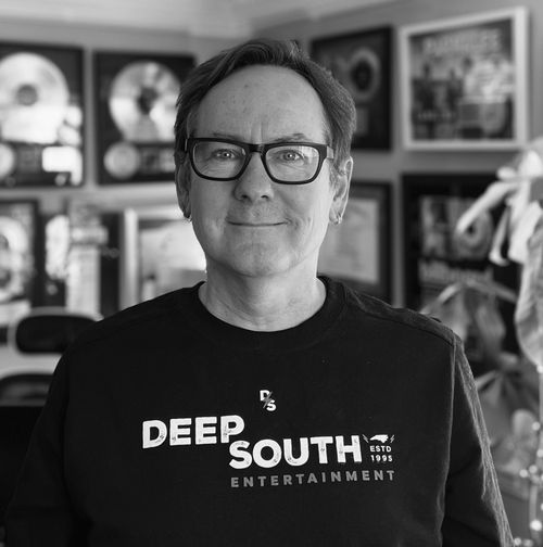 Deep South president Dave Rose, smiling and wearing glasses, standing in front of his collection of gold and platinum records