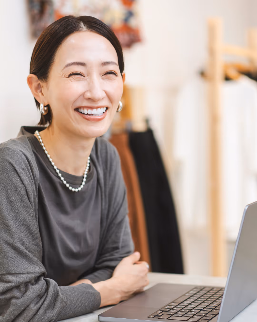 Woman in a suit, standing behind a reception desk, on the phone,  looking at a computer screen pleasantly. 