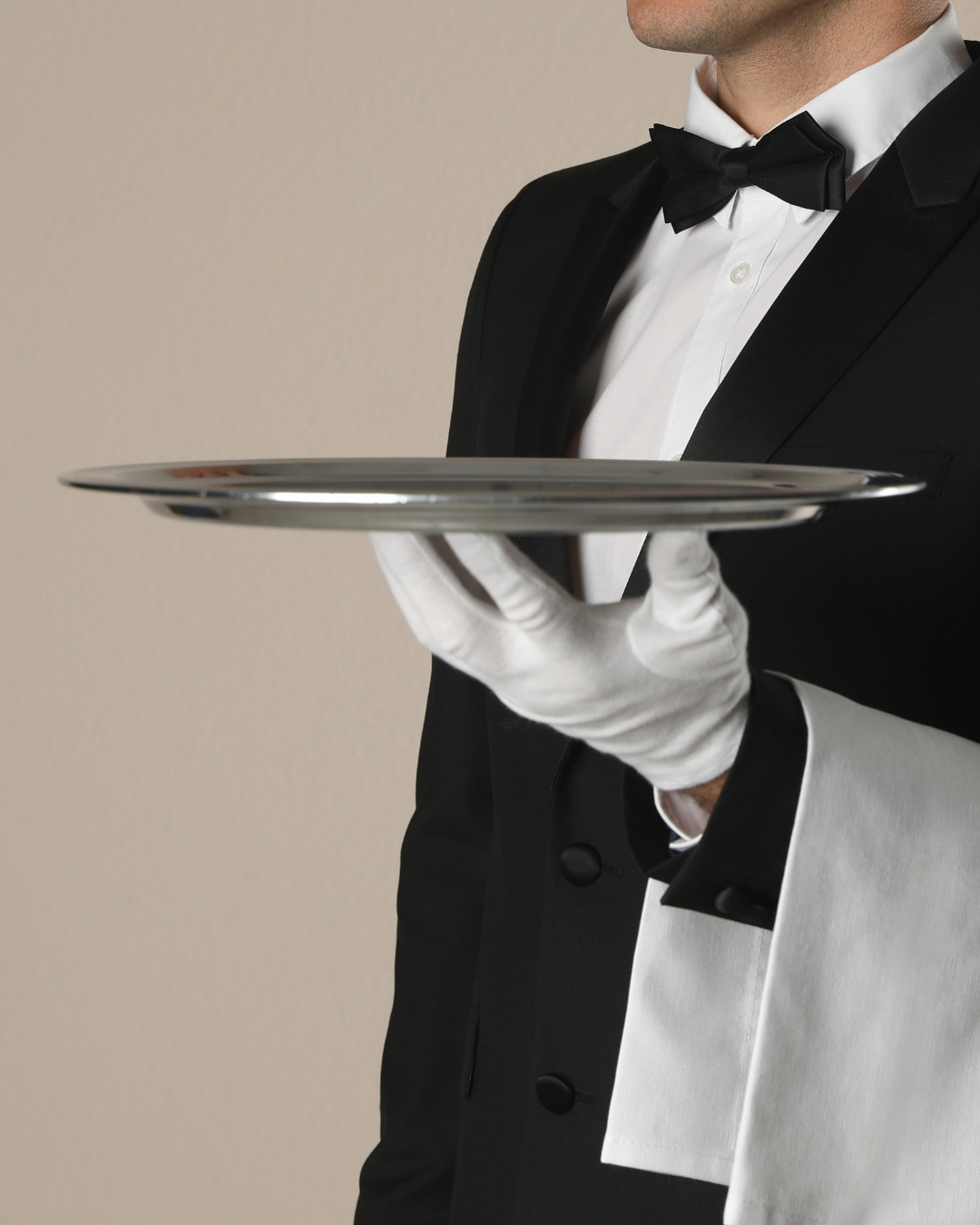 Woman in a suit, standing behind a reception desk, on the phone,  looking at a computer screen pleasantly.