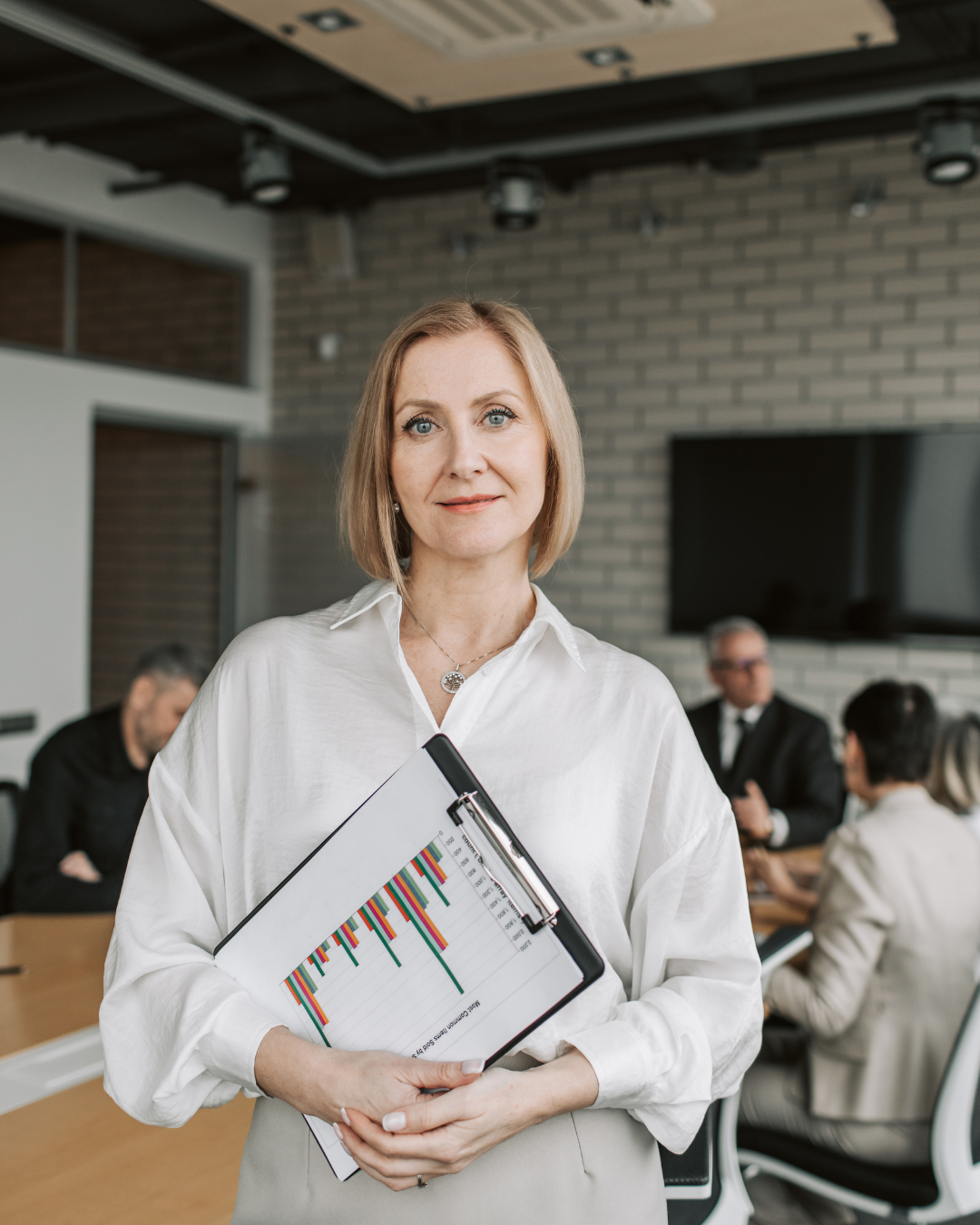 Woman in a suit, standing behind a reception desk, on the phone, looking at a computer screen pleasantly.