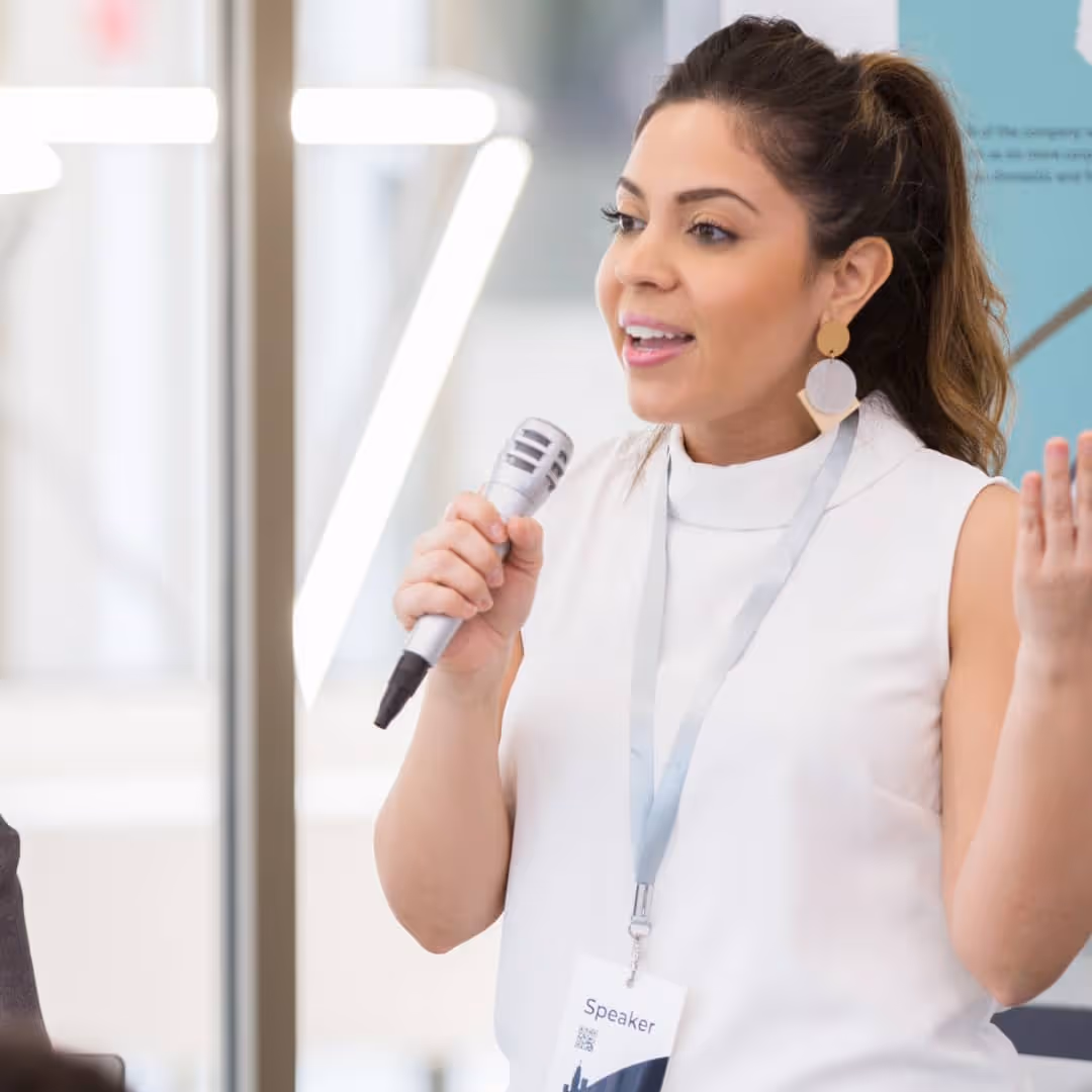 Woman at an event with a speaker pass on and holding a mic.