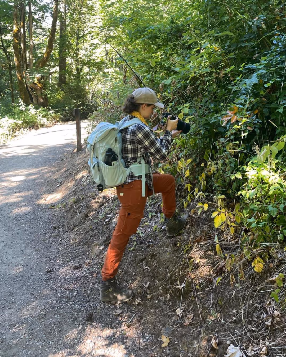 Kayla with a backpack and camera standing along a forest trail, photographing foliage.