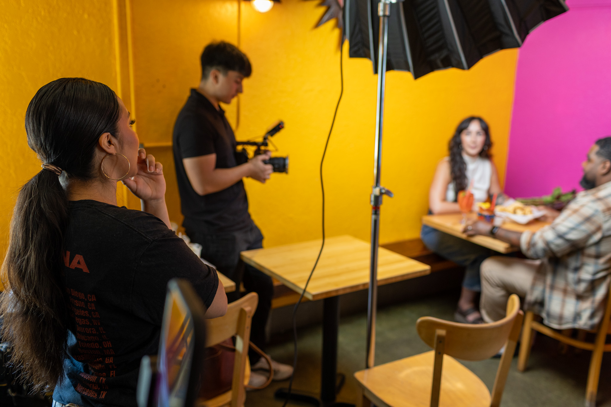 A latina woman directing a video shoot at a bright and colorful restaurant.
