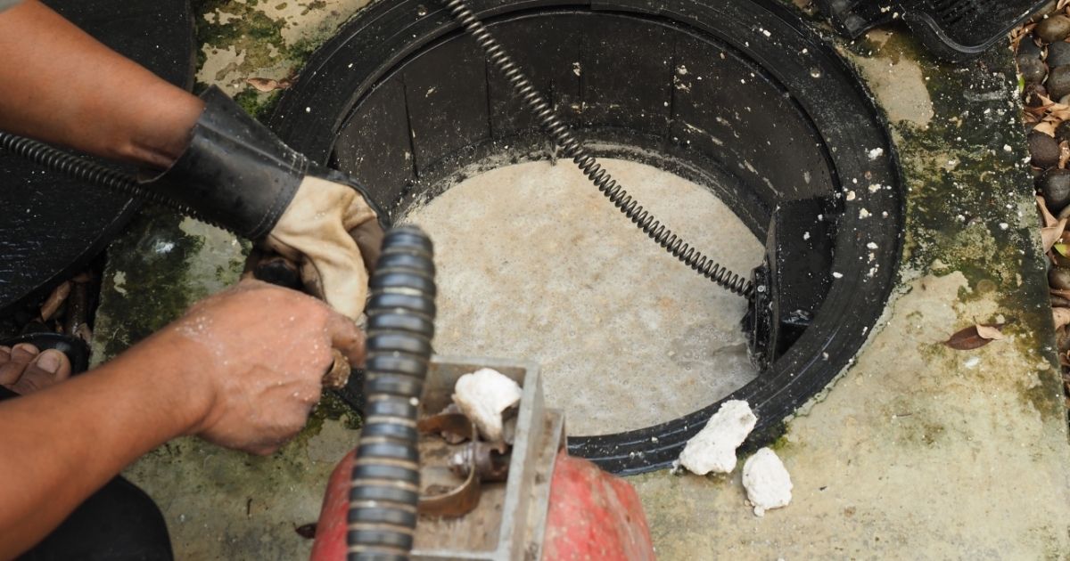 Plumber Repairing Clogged Grease Trap with Auger Machine