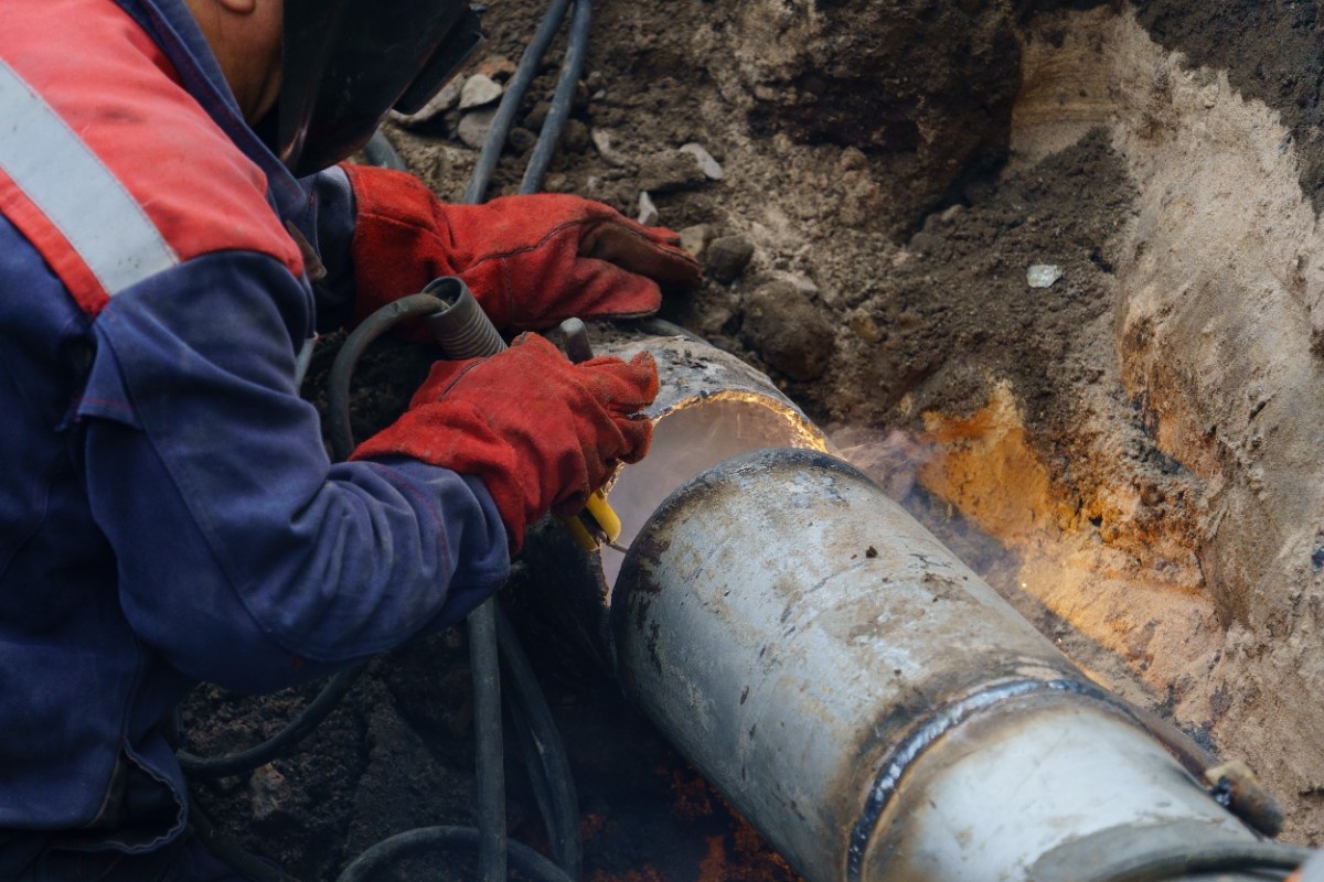 Worker connecting new PVC pipe fittings in an open trench, the traditional excavation alternative to pipe bursting vs pipe lining