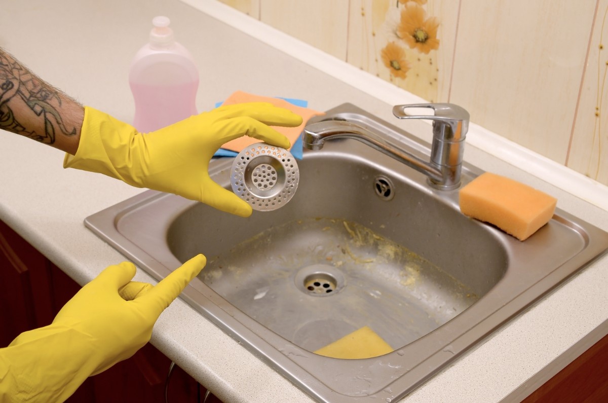Homeowner holding a dirty kitchen drain cap clogged with grease and debris