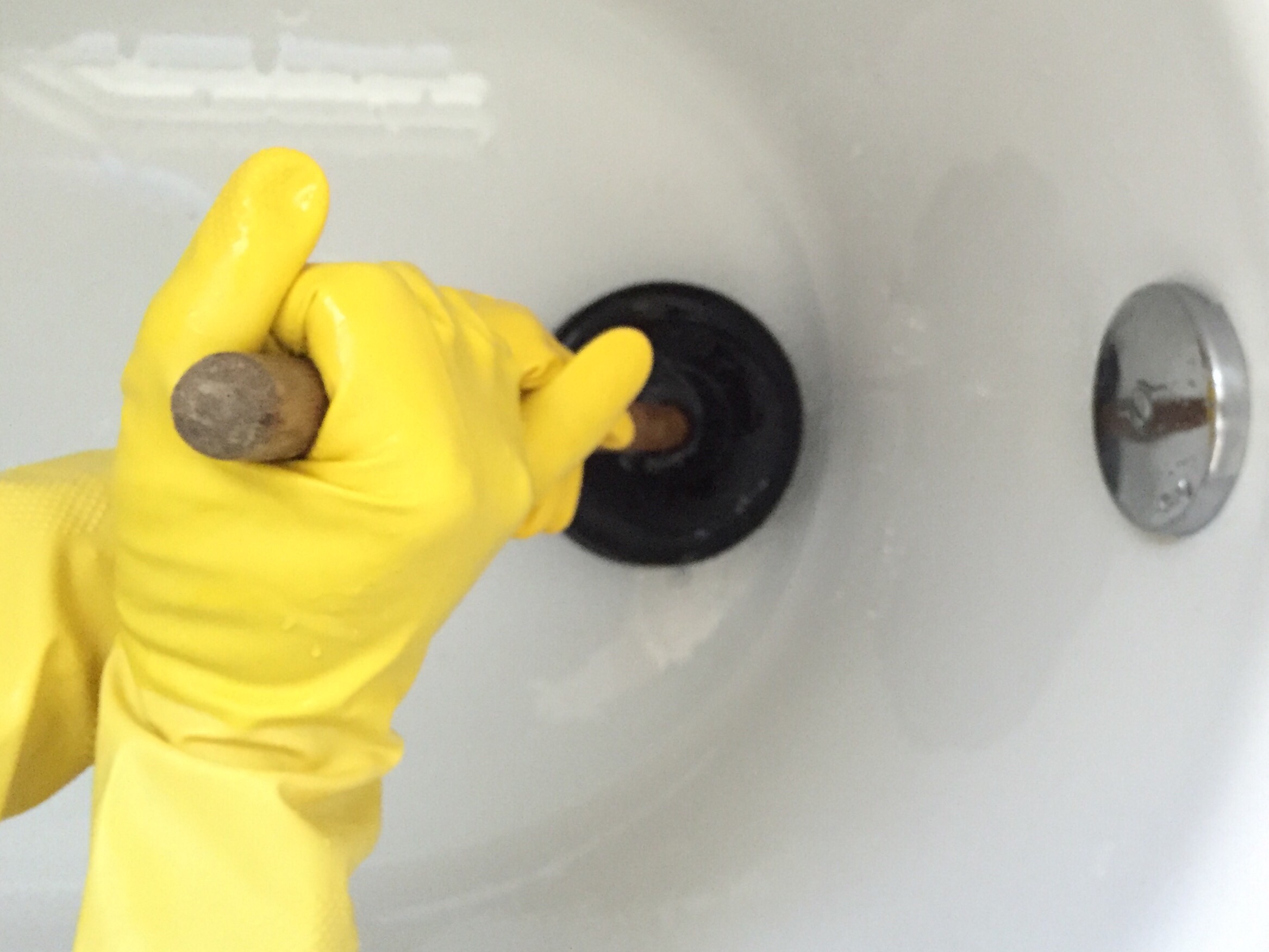 Person in yellow gloves using a plunger on a clogged bathroom drain in Seattle