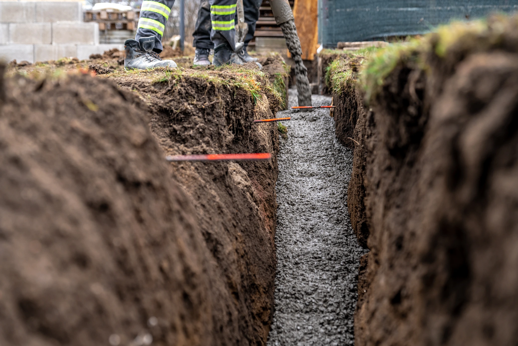 Wet concrete being poured into a deep dirt trench during foundation or underground utility work.