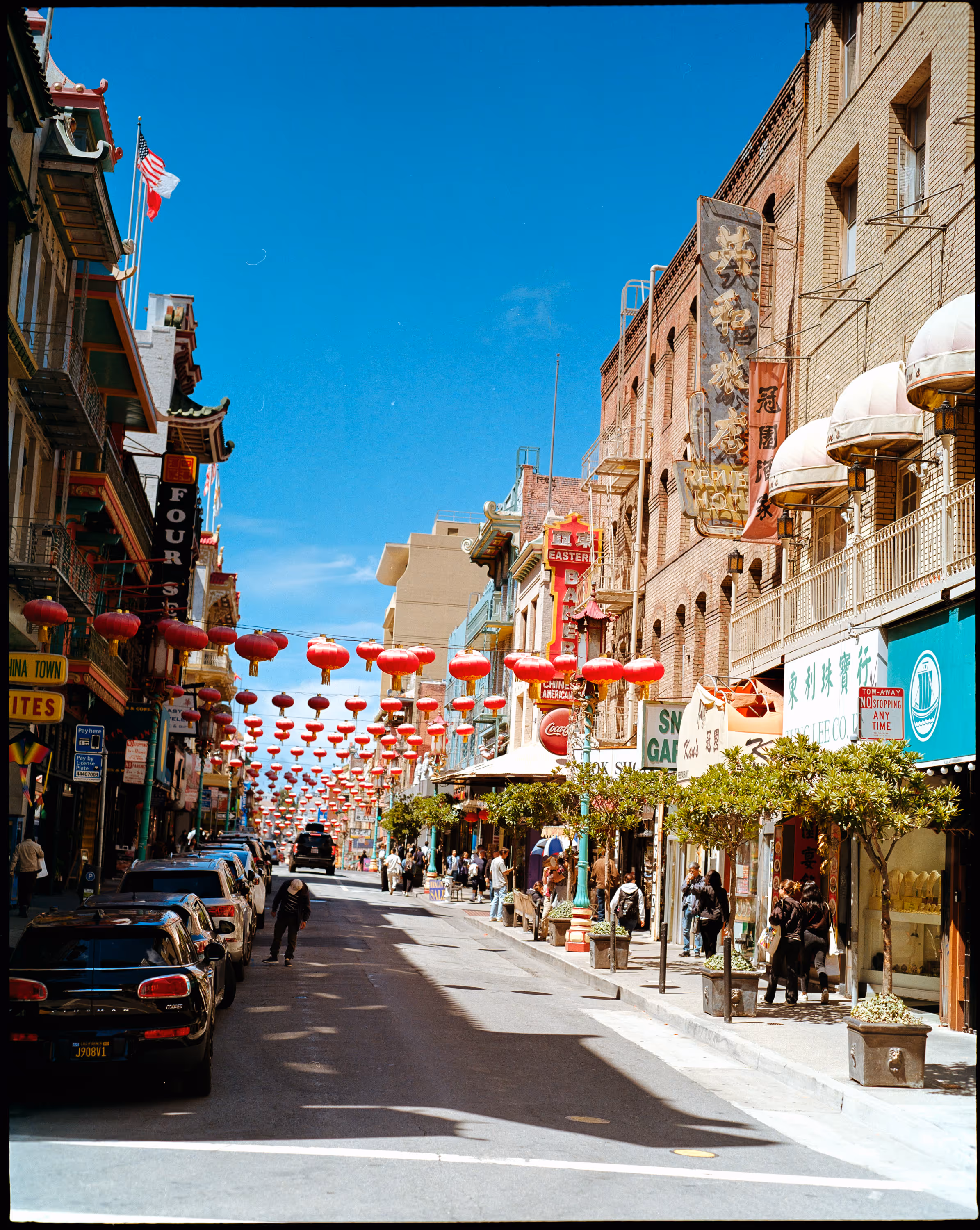 Straßenszene in Chinatown mit traditionellen roten Laternen über der Straße, Geschäften und Fußgängern bei klarem Himmel.