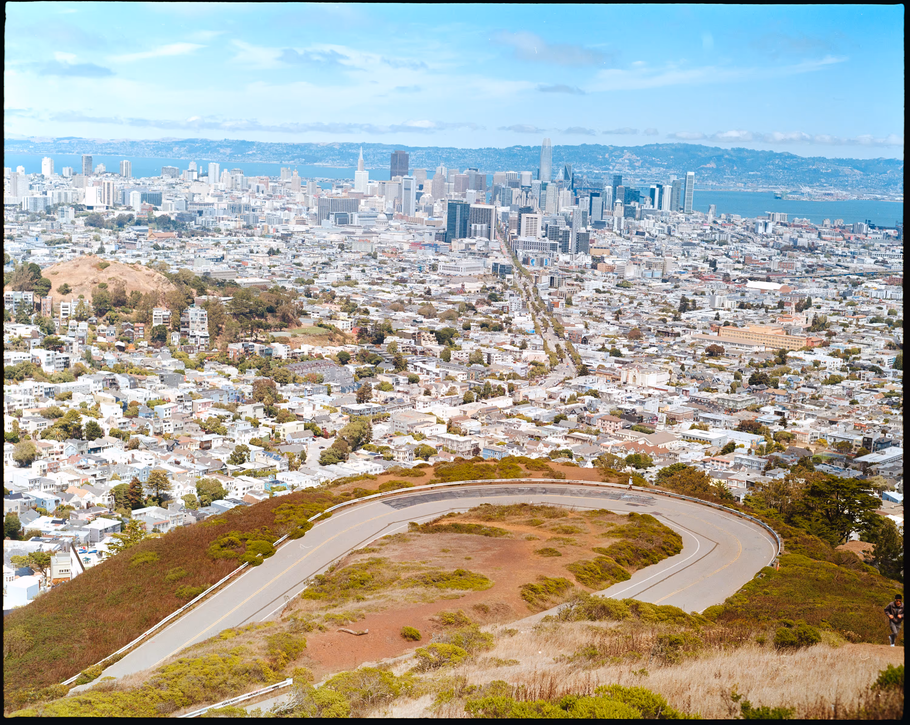 Panoramablick auf die Skyline von San Francisco mit kurviger Straße im Vordergrund und dichter Wohnbebauung.
