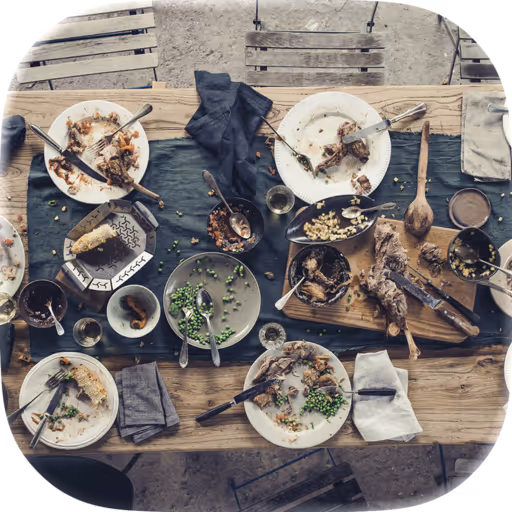 Ein Esstisch mit benutztem Geschirr, halb gegessenen Speisen und Besteck nach einer Mahlzeit im Freien.