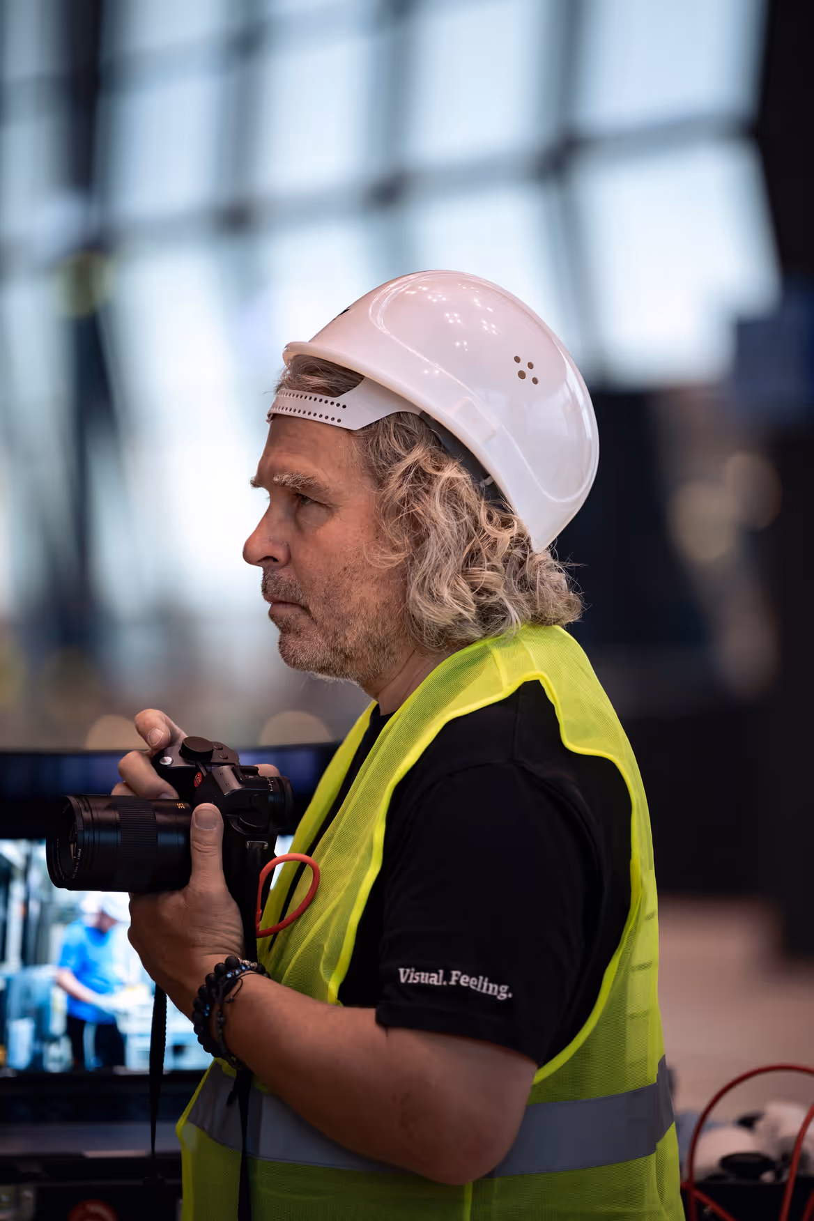 Drei lächelnde Männer stehen im Freien in der Sonne vor Bäumen, einer trägt eine Sonnenbrille.