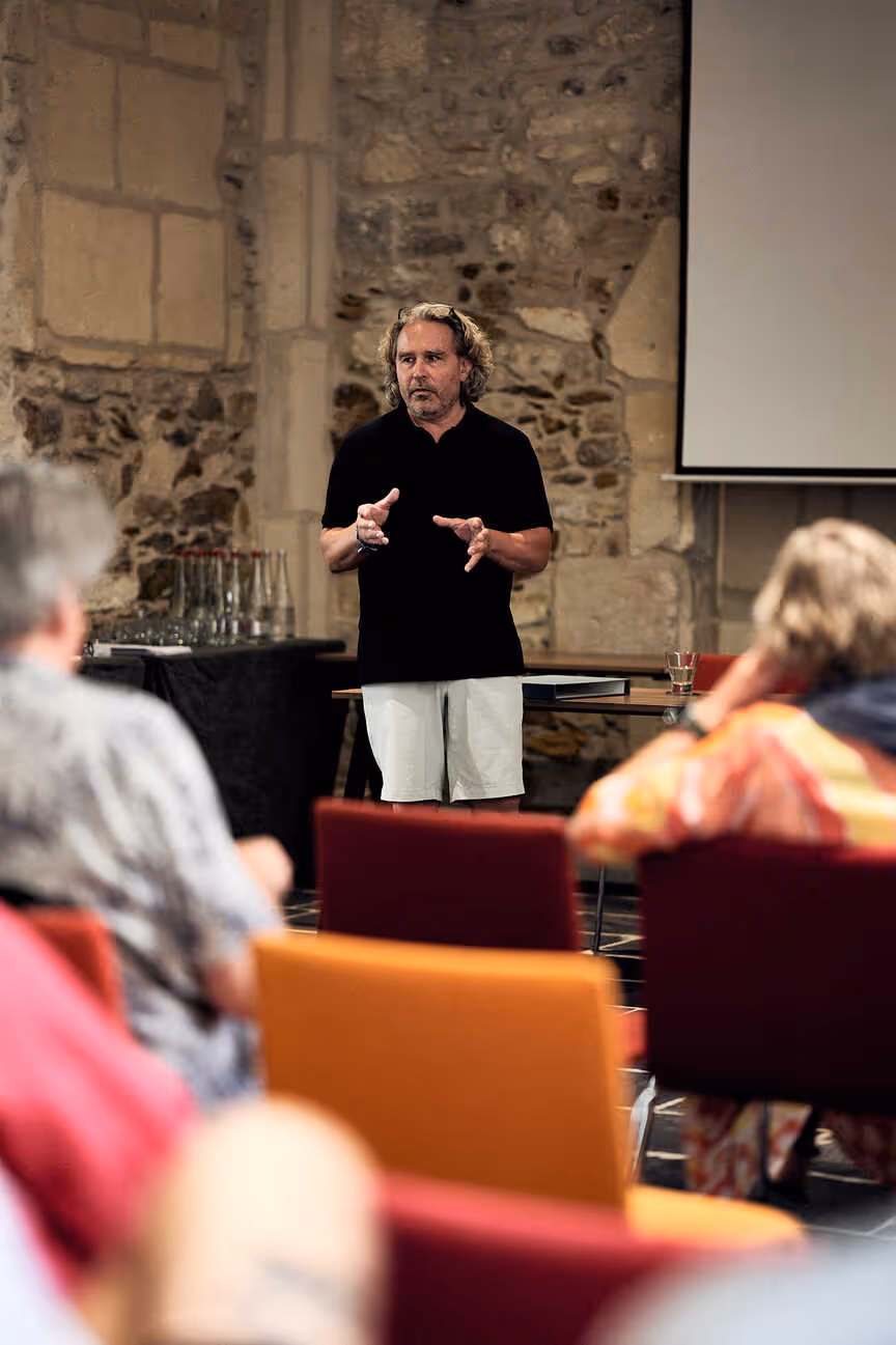 Zwei Männer in Outdoor-Bekleidung vor einem metallenen Gipfelkreuz im Schnee, einer trägt Stirnband, beide lächeln.