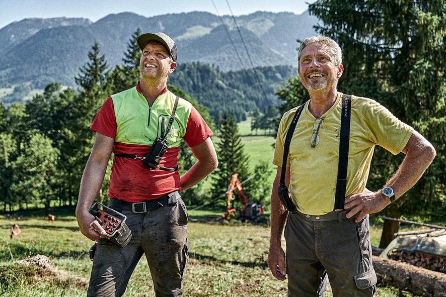 Zwei lächelnde Forstarbeiter mit Funkgeräten im Bergwald stehend.