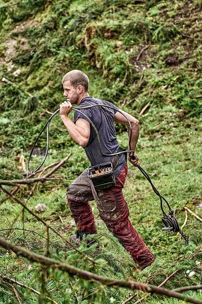 Waldarbeiter trägt Stahlseil durch bewaldete Holzerntefläche.