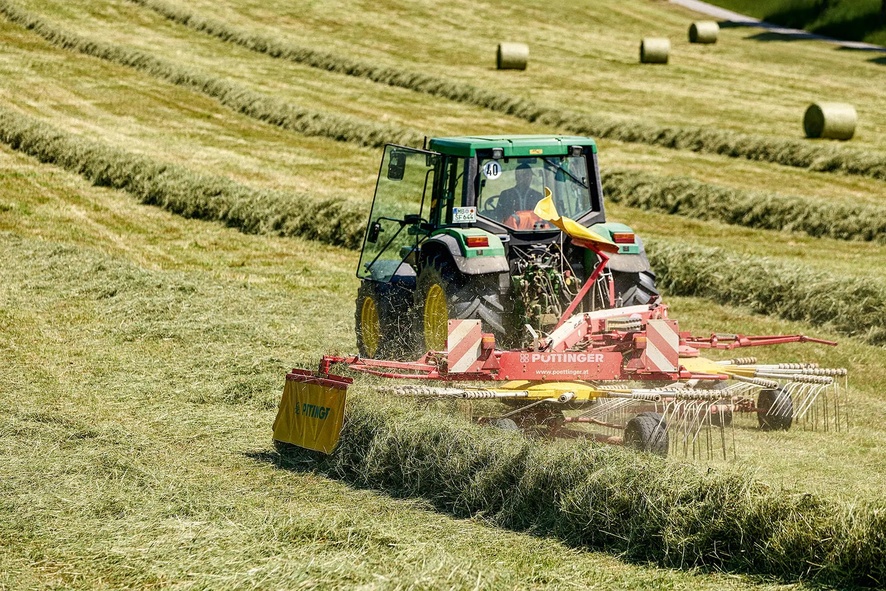 Heckansicht eines Traktors mit Schwader beim Graszusammenrechen.