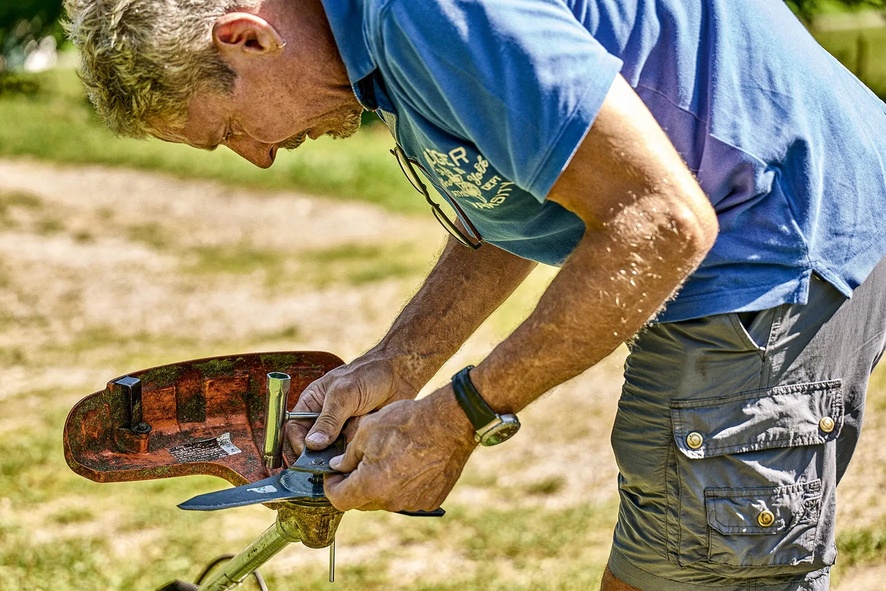 Mann schärft Freischneiderklinge im Freien bei Sonnenschein.