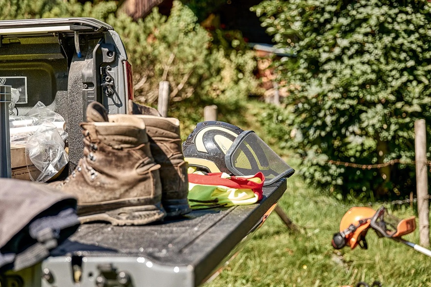 Schutzausrüstung und Wanderstiefel auf Pickup nahe Alpeneinsatz.