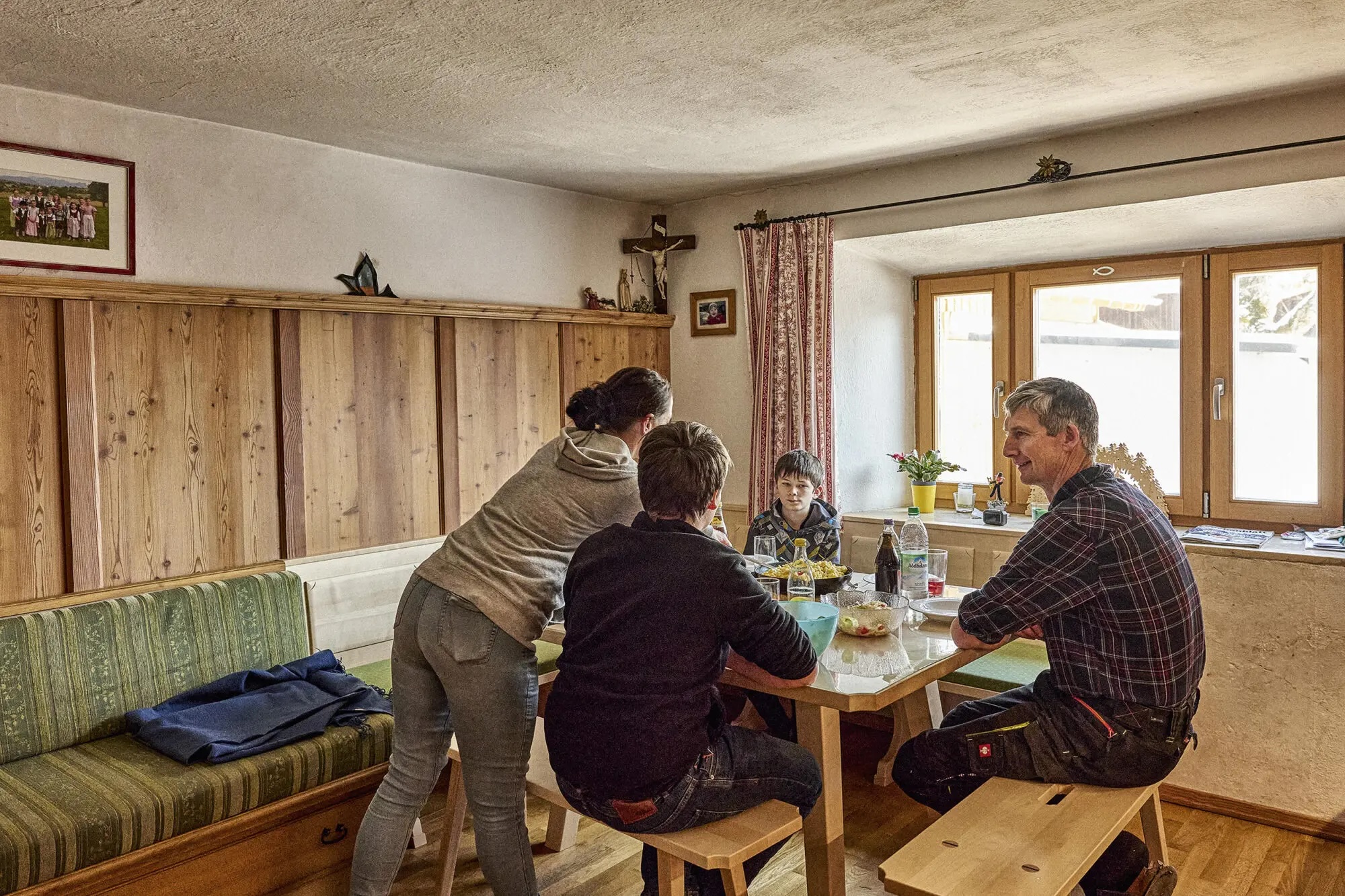 Vier Personen sitzen um einen Holztisch in einem rustikalen Zimmer mit Fenster und Holzwänden.