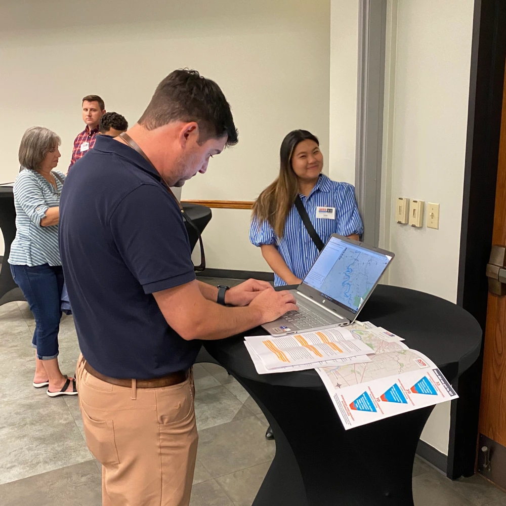 A community member answers an online map-based survey on a laptop at a public event.