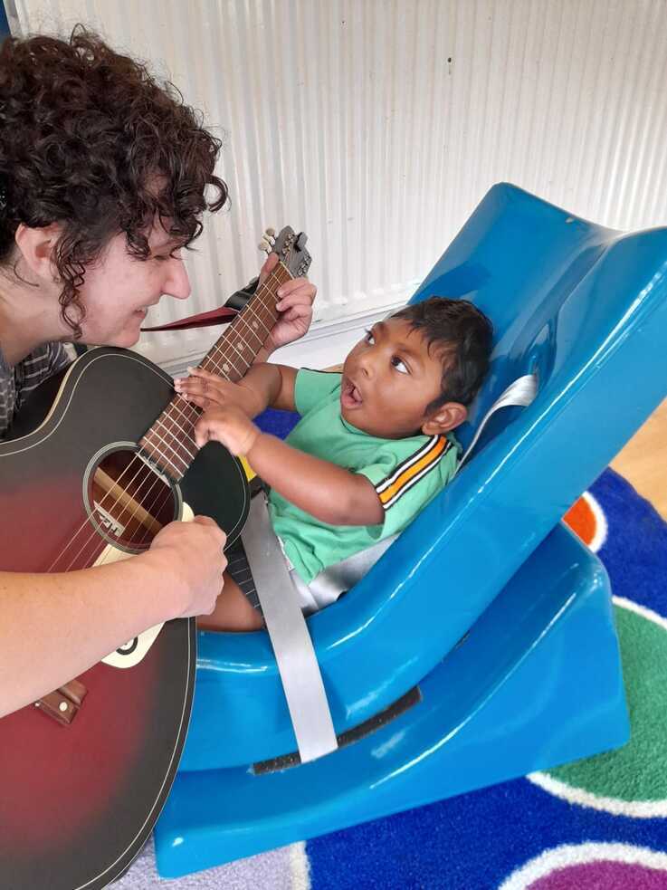 A child pulling on the strings of a guitar that a music therapist is holding