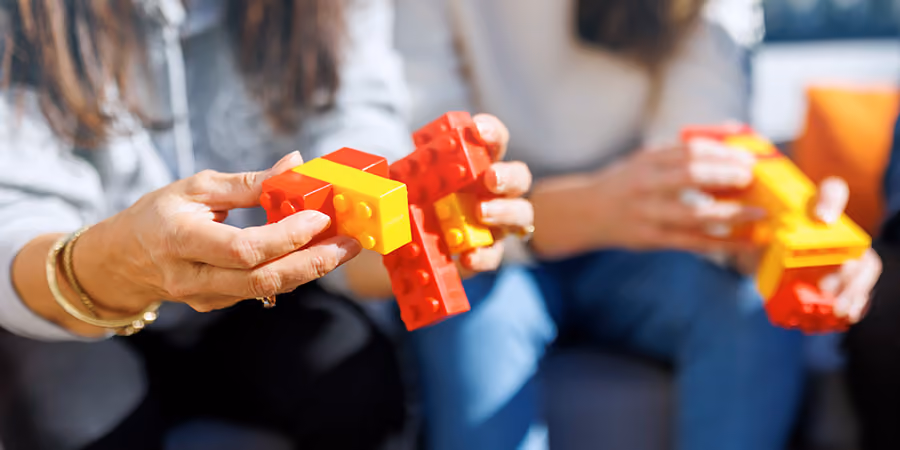 Zwei Personen halten rote und gelbe Bausteine in den Händen, Fokus auf den Händen.