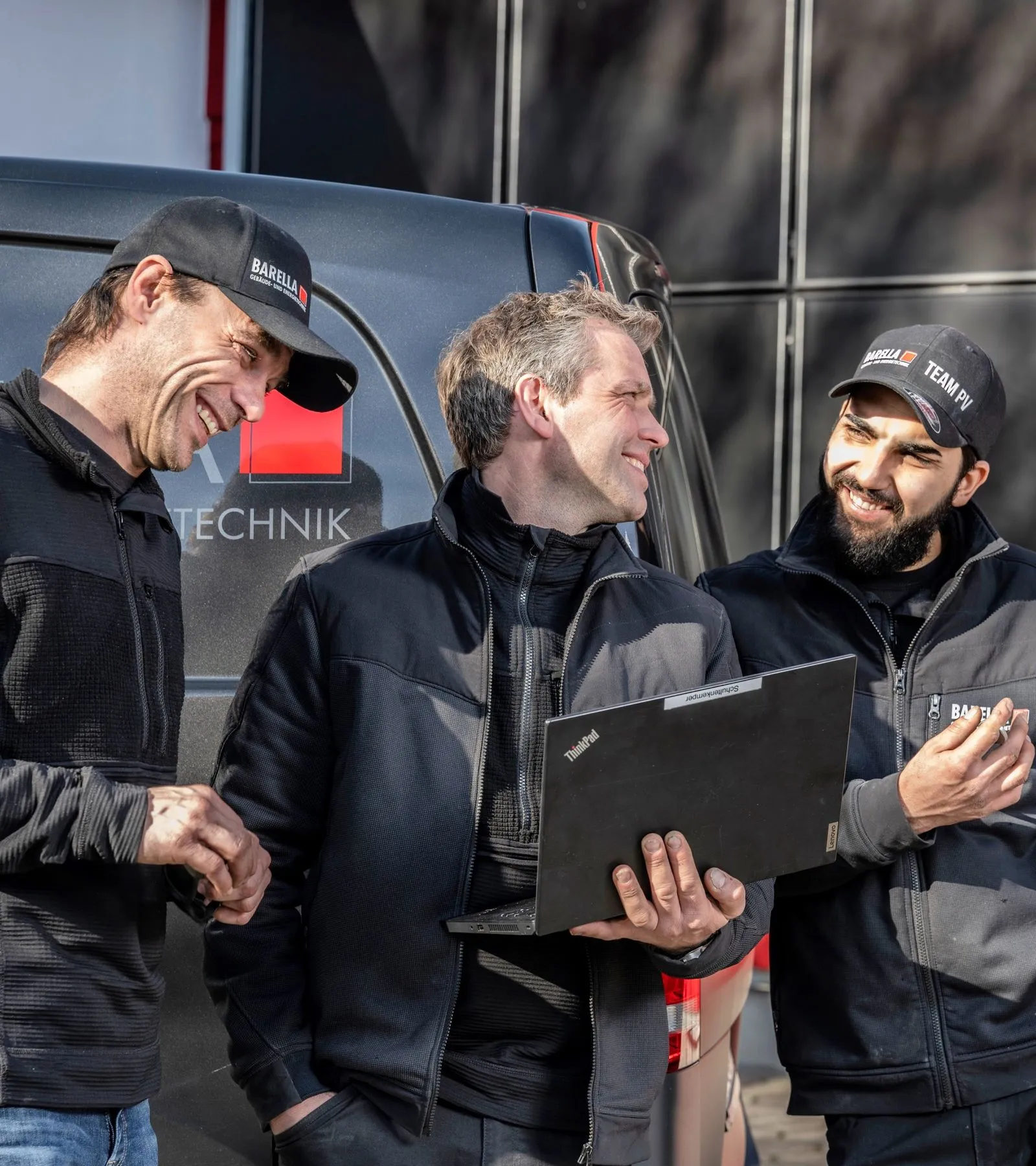 Drei Barella Mitarbeiter überprüfen Laptop vor Transporter.
