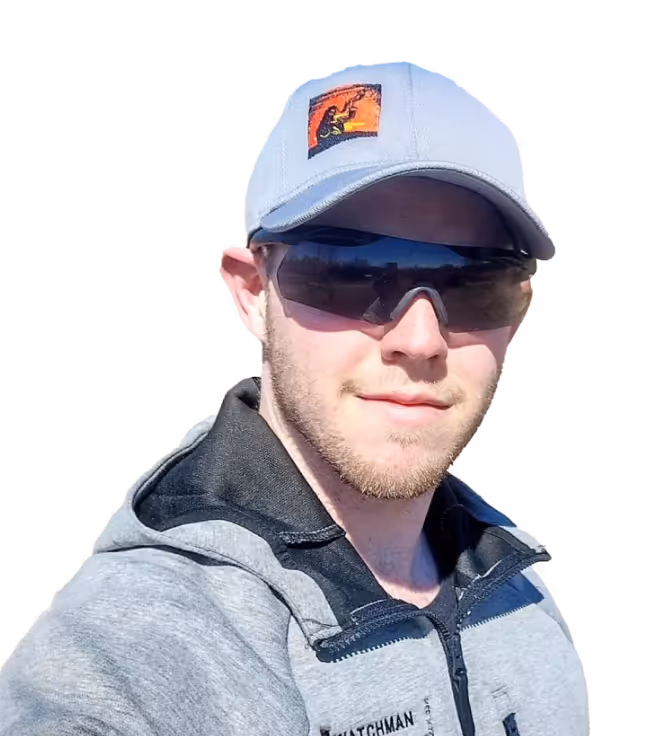 Man wearing a gray cap with a patch, dark sunglasses, and a gray and black zip-up jacket.