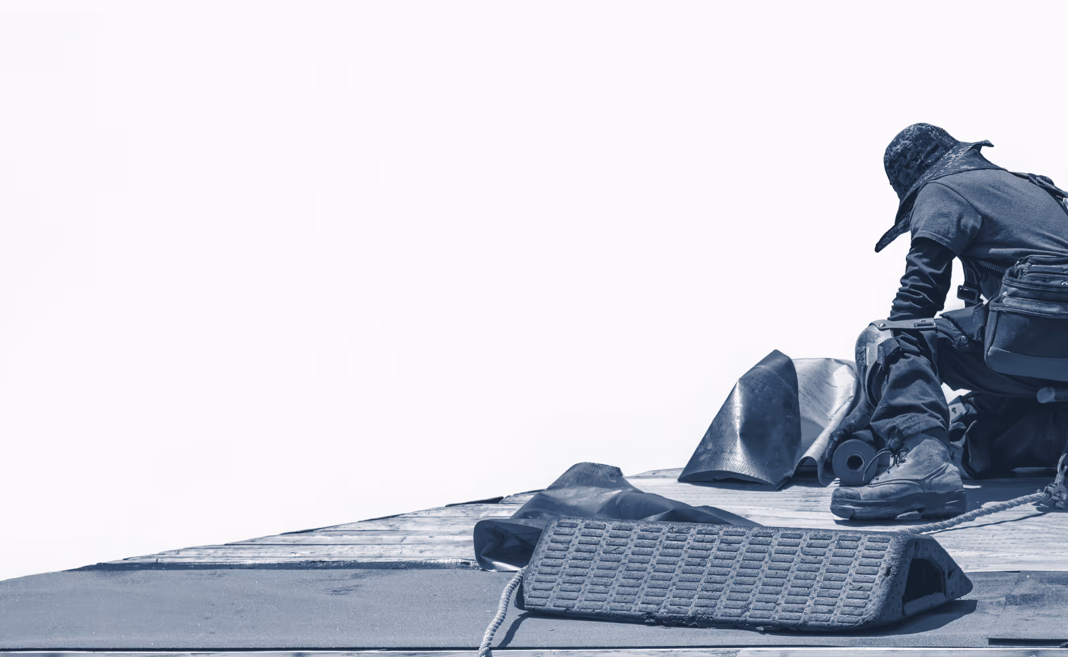 Worker in protective gear kneeling on a rooftop, handling roofing materials and tools.