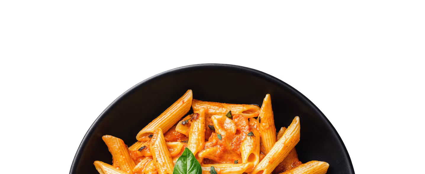 Black bowl filled with penne pasta in creamy tomato sauce garnished with basil leaf.