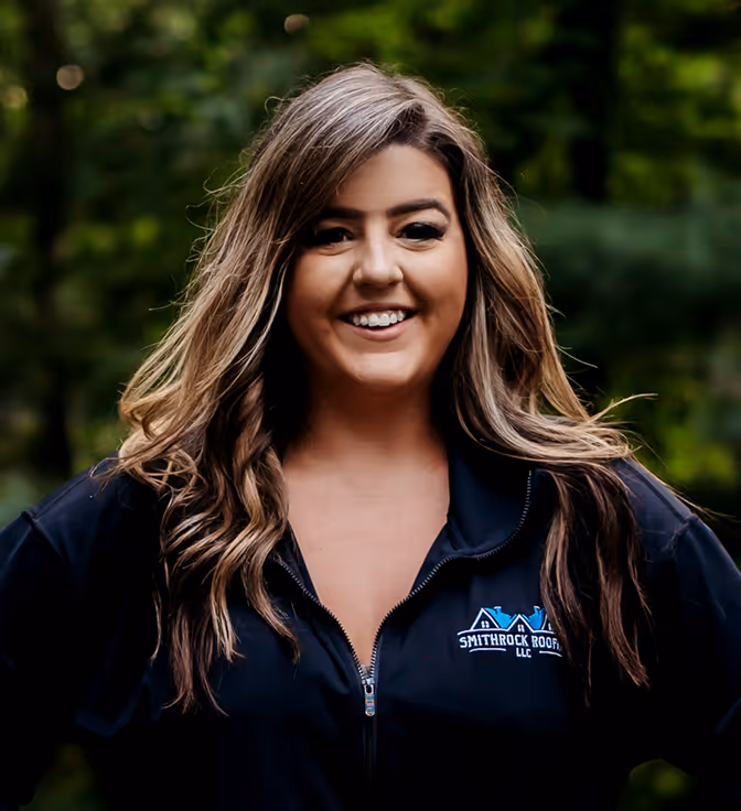 Smiling woman with long hair wearing a black jacket with Smithrock Roofing LLC logo outdoors.