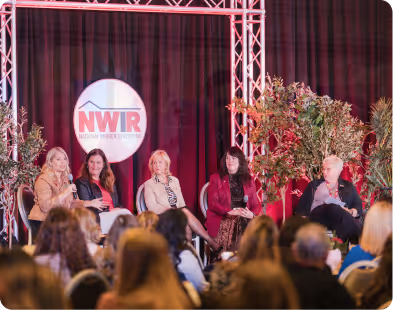 Panel of five women seated on stage at National Women in Roofing event with audience in foreground.